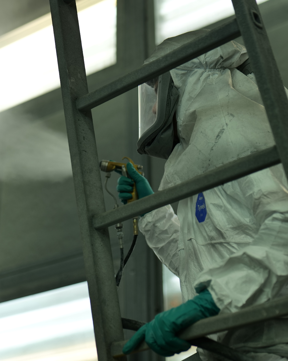 Mensch in Schutzkleidung sprüht Farbe